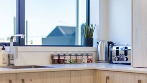 Una cocina con ventana, una planta, un hervidor, un tostador y frascos con condimentos.