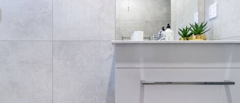 Un baño moderno con baldosas grises, un tocador blanco, un espejo y una planta pequeña en la encimera.