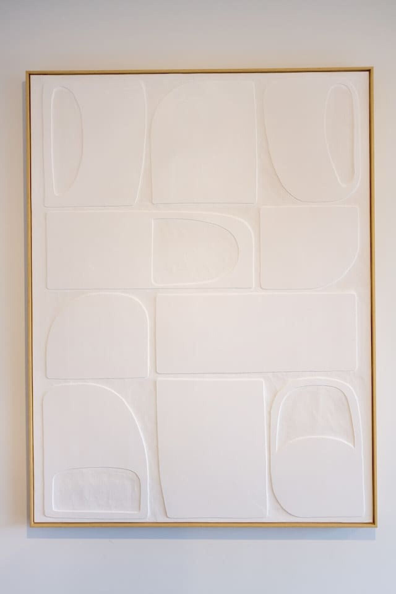 A framed abstract artwork with geometric shapes on a plain wall.