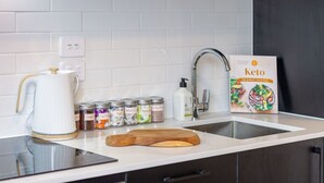Una cocina moderna con azulejos blancos, electrodomésticos de acero inoxidable, un hervidor, frascos de especias y un libro de cocina cetogénica.