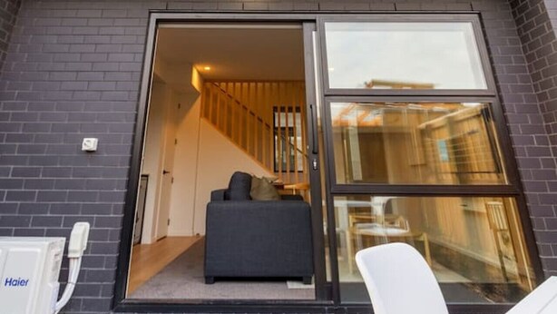 Un edificio moderno con un amplio acceso por puerta de vidrio que conduce a una sala de estar con un sofá y una mesa de comedor.