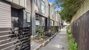 Un sendero estrecho bordeado por casas modernas, con una cerca de metal a un lado y una de madera al otro.
