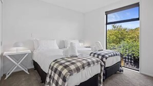 Un dormitorio moderno con dos camas, un escritorio y un ventanal con vistas a la vegetación.