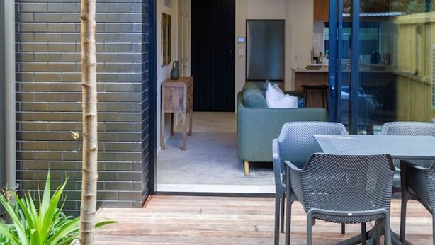 Un patio moderno al aire libre con una mesa de comedor y sillas, una planta pequeña en maceta y vistas a un espacio interior contemporáneo.