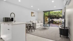 Una cocina moderna con microondas, una zona de comedor con sofá y sillas, y un amplio ventanal corredero que da a un jardín.