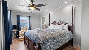 Une chambre avec un grand lit, un ventilateur de plafond, une chaise, une lampe et un téléviseur.