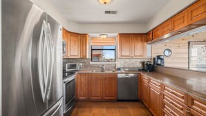 Een moderne keuken met houten kasten, roestvrijstalen apparatuur en uitzicht op het strand door het raam.