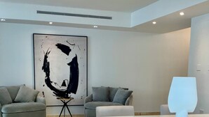 Una sala de estar moderna con dos sofás grises, una mesa de centro blanca y un cuadro abstracto grande en la pared.