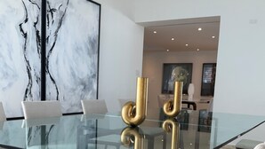 Un comedor moderno con una mesa de vidrio, cuatro sillas y un cuadro abstracto grande en la pared.