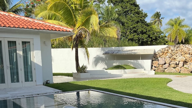 Una piscina con borde de piedra, rodeada por un césped cuidado y palmeras.