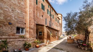 Une ruelle étroite bordée d’un immeuble en briques, de plantes en pot et d’un arbre.