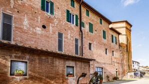 Un bâtiment en briques doté de nombreuses fenêtres et volets, une cour avec des plantes en pot et un ciel dégagé.