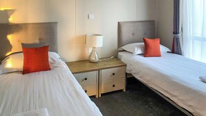A hotel room with two beds, a nightstand with a lamp, and a window with curtains.