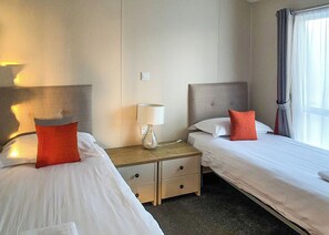 Ein Hotelzimmer mit zwei Betten, einem Nachttisch mit Lampe und einem Fenster mit Vorhängen.
