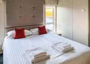 Hotellihuone, jossa on suuri sänky, kaksi punaista tyynyä, sängynpääty, yöpöytä ja ikkuna, josta on näkymä.