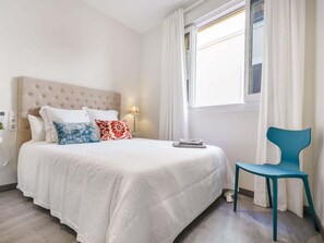 A hotel room with a bed, a chair, a lamp, and a window with curtains.
