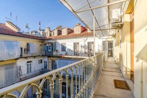 Un balcon abrité avec une rambarde en métal, un ciel dégagé et des bâtiments aux toits recouverts de tuiles rouges.