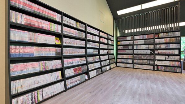 A library with multiple bookshelves filled with books, a wooden floor, and a large window allowing natural light.