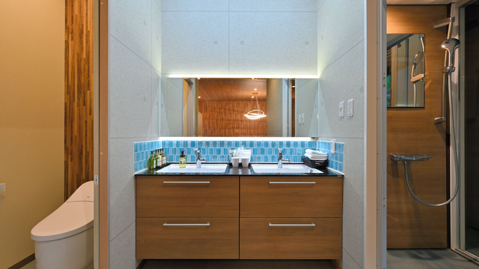A modern bathroom with a wooden vanity, a glass shower enclosure, and a blue-tiled sink area.
