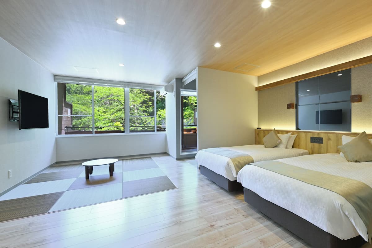 A modern hotel room with two beds, a large window, a flat-screen TV, and a small table.