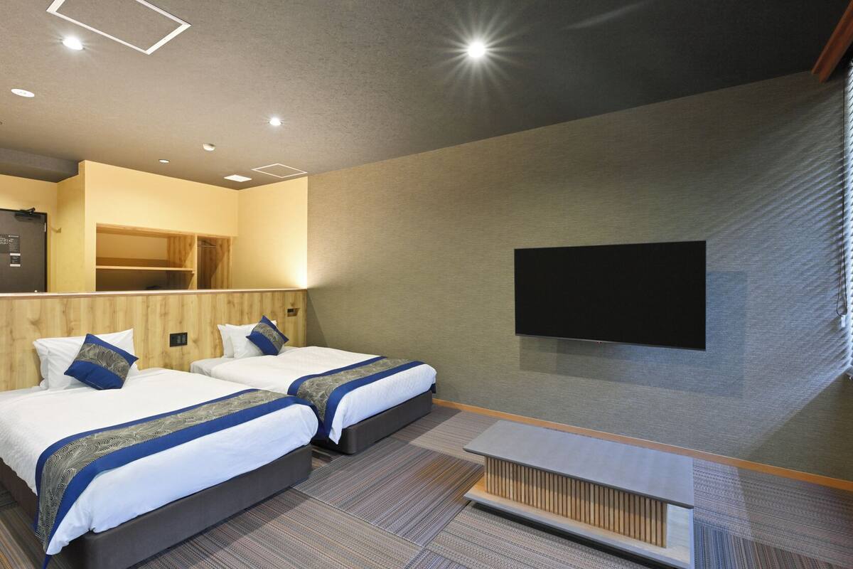 A hotel room with two beds, a TV mounted on the wall, and a small table.