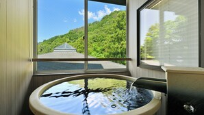 Un baño con bañera, una ventana que ofrece vistas a una casa y un bosque, y una zona de ducha.