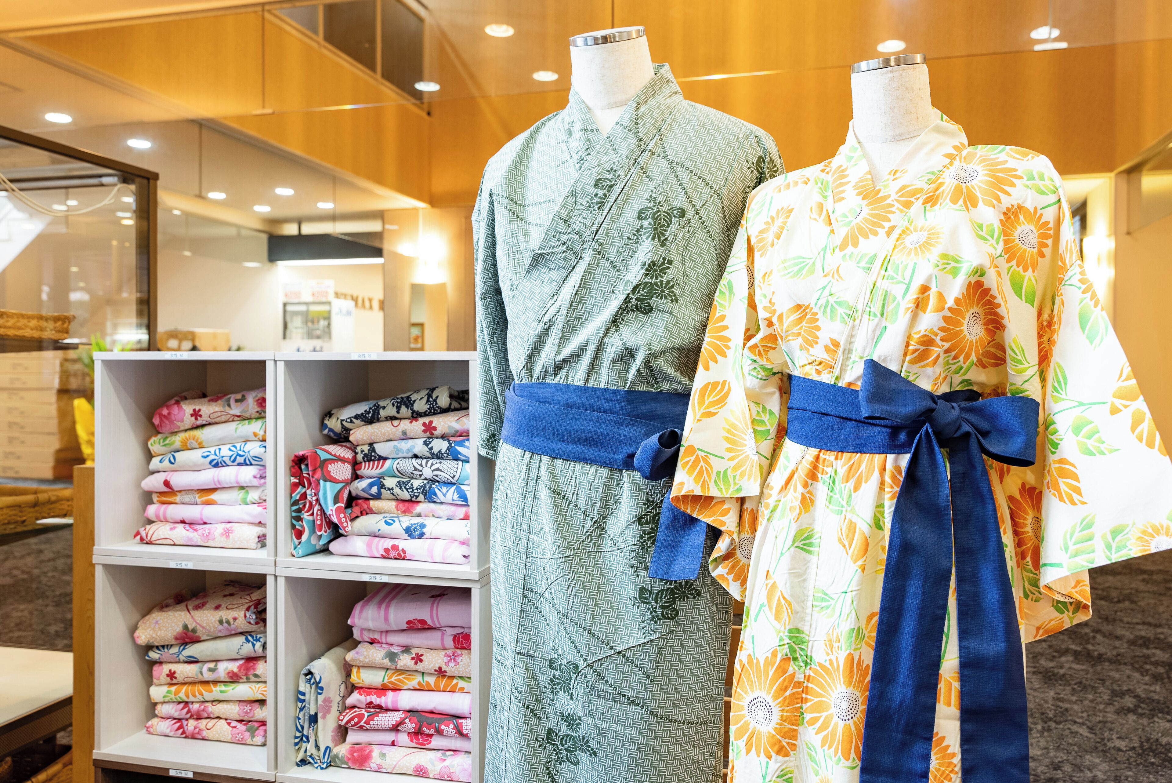 Dos maniquíes vestidos con trajes tradicionales, un estante con telas dobladas y un interior de madera.