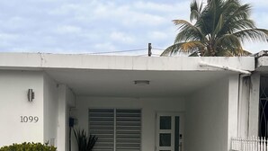 Un edificio moderno con fachada blanca, el número '1099' en la pared, una pequeña entrada con una puerta y una planta en maceta.