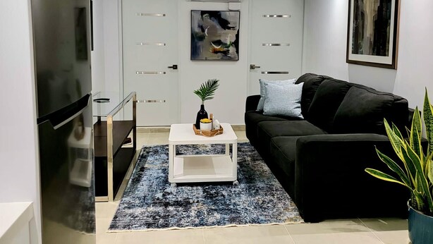 Una sala de estar moderna con un sofá negro, una mesa de centro blanca, un televisor y un cuadro en la pared.