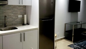 Una cocina moderna con armarios blancos, un refrigerador de acero inoxidable, un microondas integrado y un televisor de pantalla plana montado en la pared.