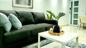 Una sala de estar moderna con un sofá verde oscuro, dos cojines grises, una mesa de centro blanca y un jarrón con plantas.