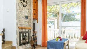 Ein Wohnzimmer mit Kamin, einem Tisch mit Früchten und einem Balkon mit Blick auf Bäume.