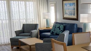 Un salon avec un canapé bleu, des fauteuils gris, une table basse en bois et une table à manger avec des chaises.