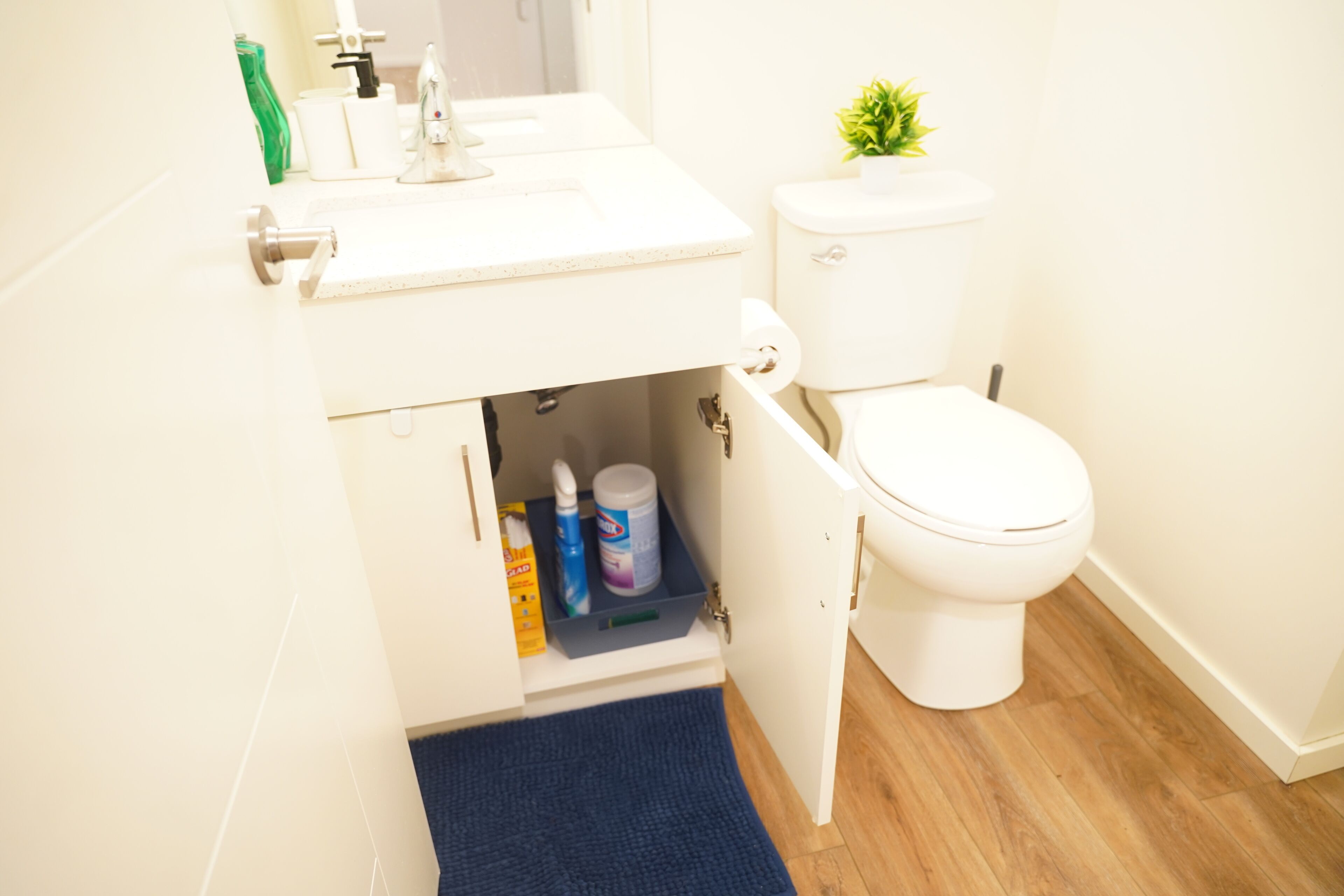 A bathroom with a white sink, toilet, and a cabinet with cleaning supplies.