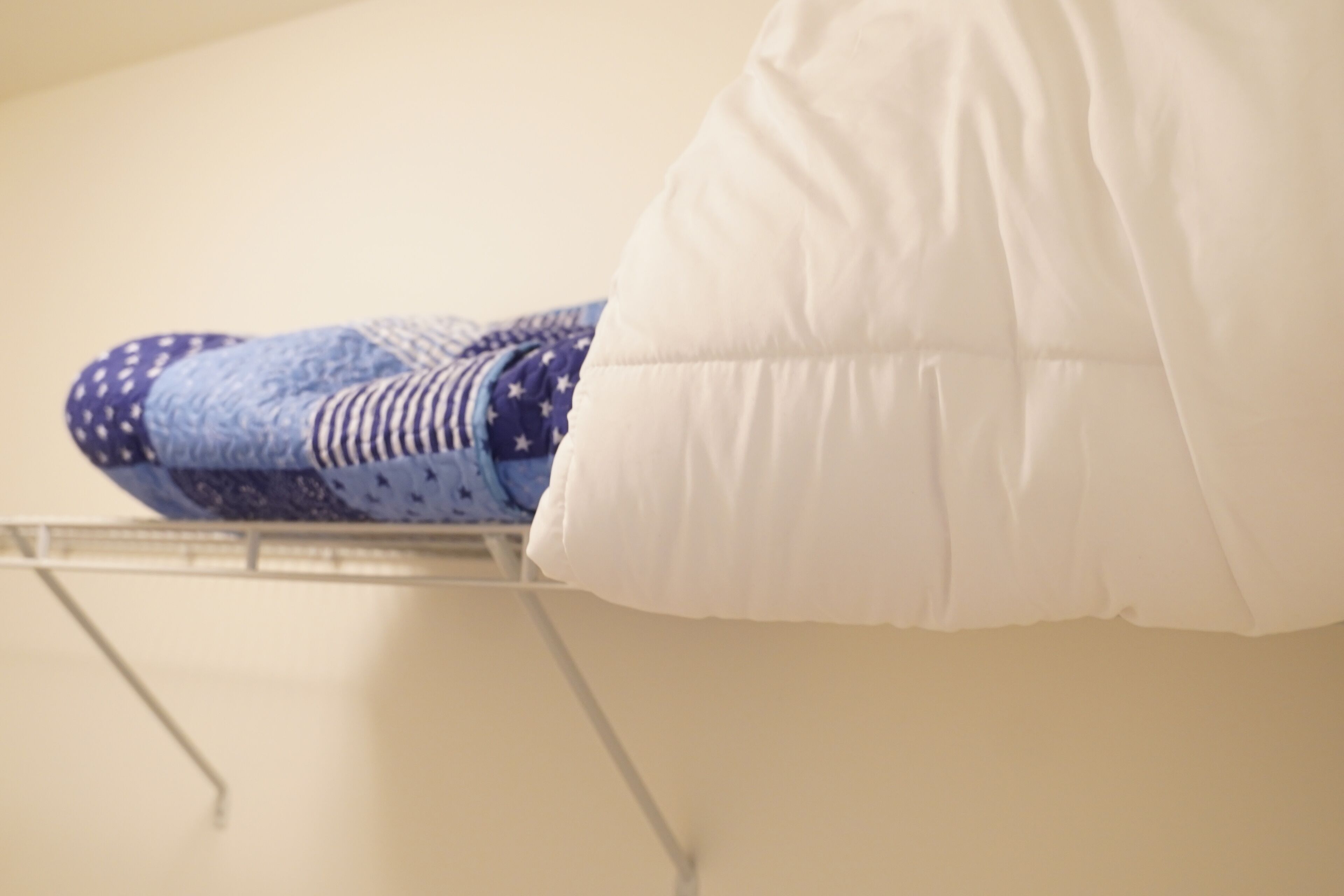 A bed with a white pillow and a blue patterned blanket.