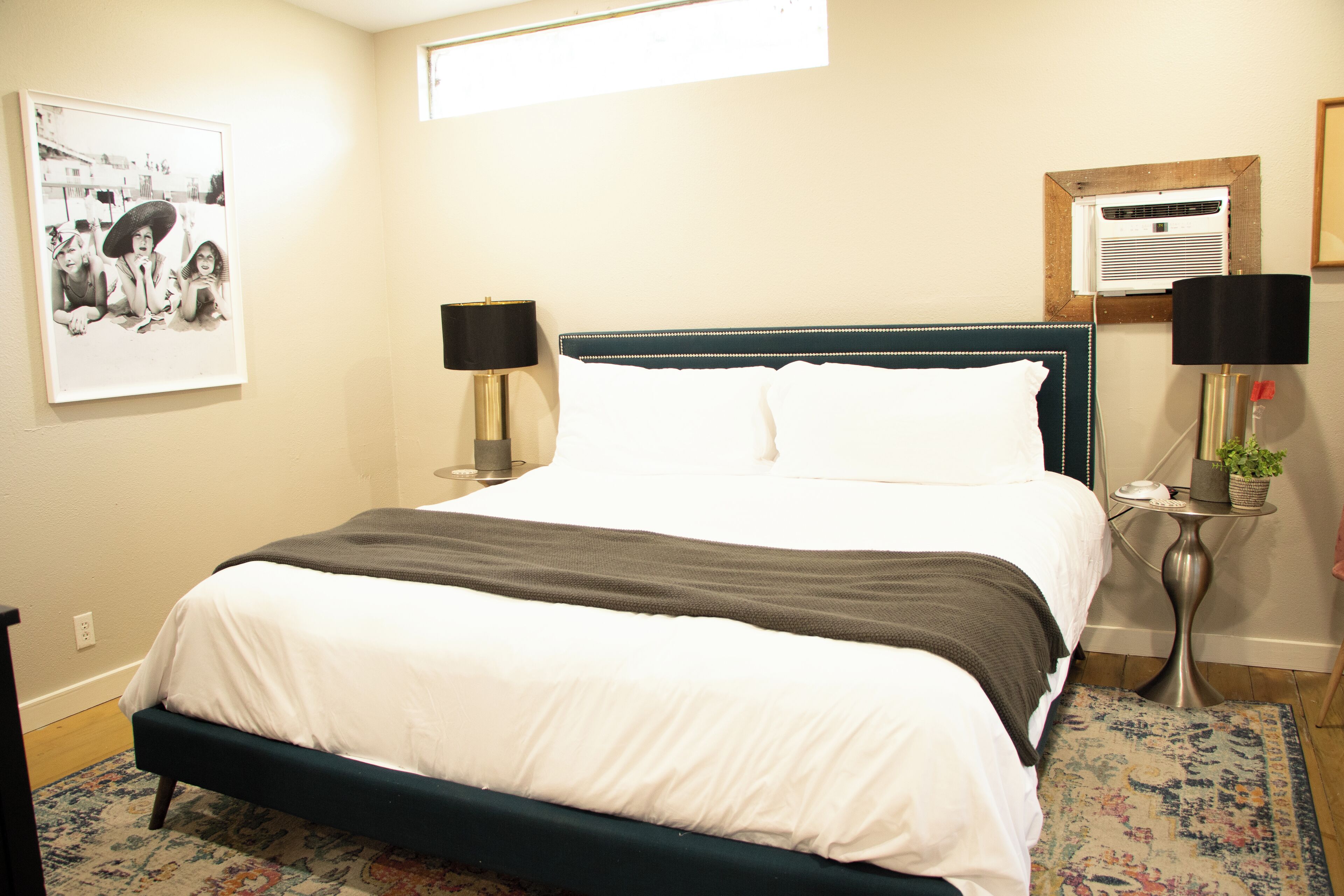A neatly made bed with white and gray bedding, a dark blue headboard, and a small bedside table with a lamp.