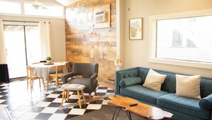 A living room with a checkered floor, a blue sofa, a wooden coffee table, a grey armchair, and a dining table with chairs.