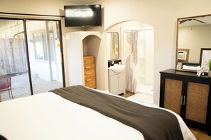Une chambre à coucher avec un lit, un téléviseur fixé au mur, une salle de bain avec un lavabo et un miroir, et une commode en bois.