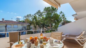 Un balcon avec une table préparée pour le petit-déjeuner, comprenant des fruits, du café et une bouteille de vin.