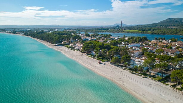 Vista aerea di una località costiera con spiaggia, case e una montagna sullo sfondo.
