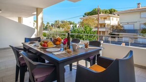Un balcone con un tavolo apparecchiato per la colazione, con frutta e una bottiglia, che si affaccia su una zona residenziale con edifici e alberi.