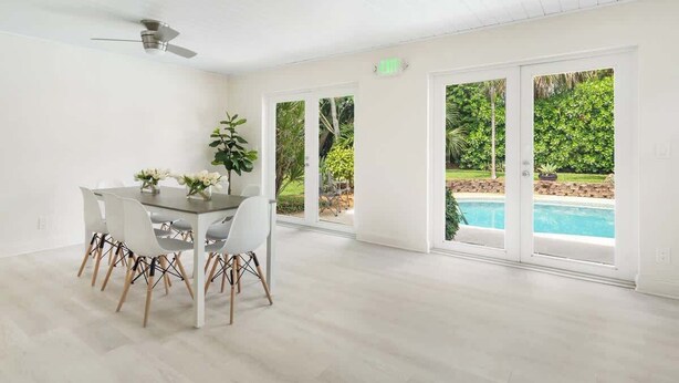 Una habitación amplia con una mesa de comedor, sillas, ventilador de techo y grandes puertas de cristal correderas que dan a una piscina.