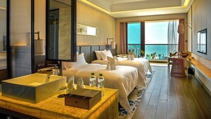 Ein Hotelzimmer mit einem großen Bett, einem Badezimmer mit einer Badewanne, einer Essecke mit Tisch und Stühlen und Meerblick.
