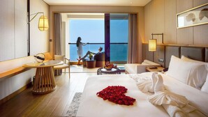 Ein Hotelzimmer mit Bett, einer Sitzecke mit Meerblick, einem Balkon und einem großen Fenster.