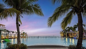 Ein Poolbereich mit Palmen, einer Rutsche und Blick auf das Meer im Abendlicht.