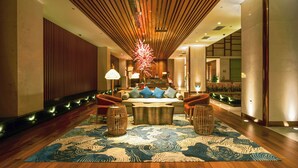 Eine moderne Lobby mit Holzboden, einer zentralen Sitzecke mit Musterteppich und einem Empfangsschalter im Hintergrund.