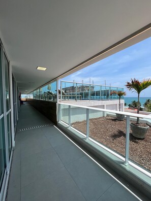 A corridor with a glass railing overlooking a pool area and a view of the sea. - Melhor Flat do Nixxus a passos da praia (Ipojuca)