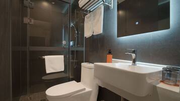 A modern bathroom with a glass-enclosed shower, a white toilet, a sink with a mirror, and a towel rack.