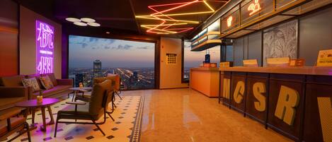 A modern hotel lobby with a city view, a reception desk, and a seating area with a patterned floor.