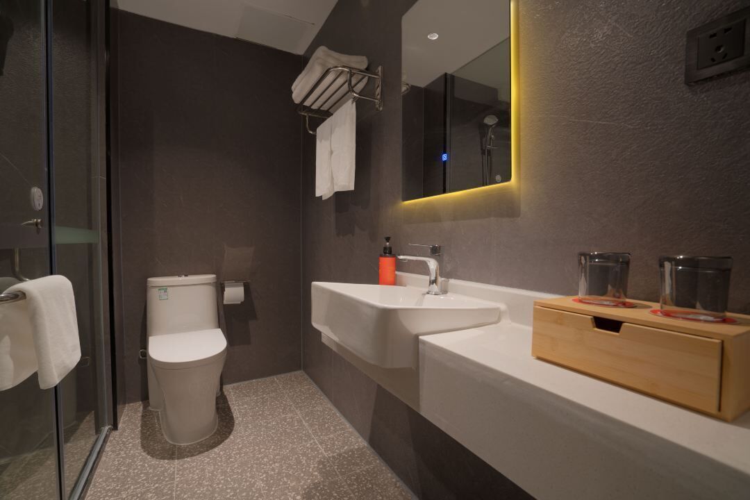 A modern bathroom with a glass shower enclosure, a white toilet, a sink with a mirror, and a wooden vanity with two glasses.